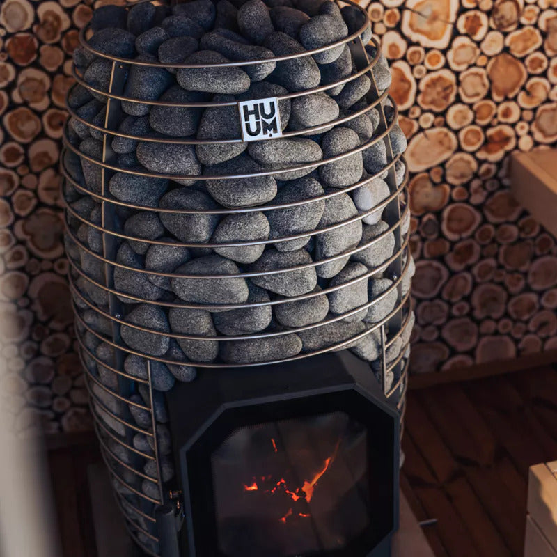 HUUM HIVE Flow Holzsaunaofen mit Steinkorb in einer rustikal eingerichteten Sauna.