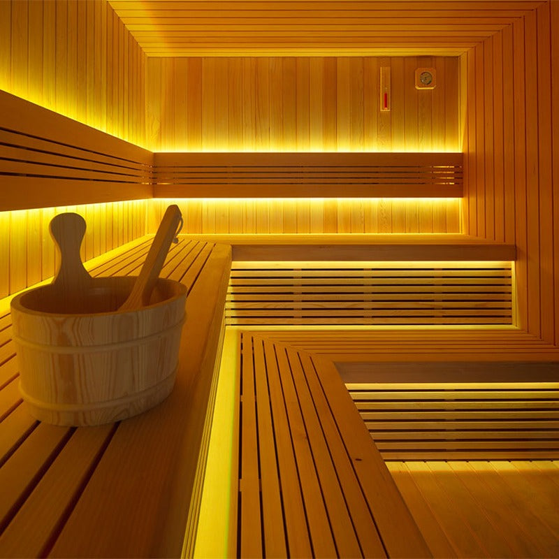 Innenansicht der AWT The Cube X7-L Hemlock Außensauna 300×235 cm mit zweistufigen Bänken, Aufgusskübel und intensiver gelber LED-Ambientebeleuchtung