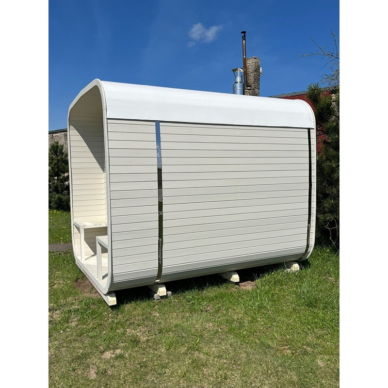 Seitenansicht der weißen Celsium Ula Large Sauna mit sanft geschwungener Dachform und überdachtem Eingangsbereich auf Rasenfläche