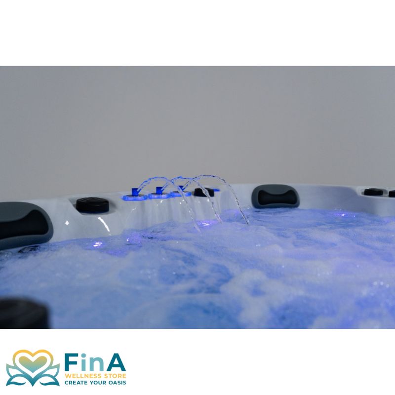 Seitliche Aufnahme des FinA Xaluna Outdoor Whirlpools mit aktiven Wasserfontänen und blauer LED-Beleuchtung, umgeben von ergonomischen Kopfstützen.