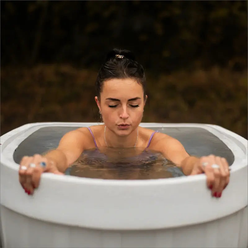 Junge Frau sitzt entspannt im Eisbad in stilvoller Umgebung, umgeben von Natur.🌿🧘♀️