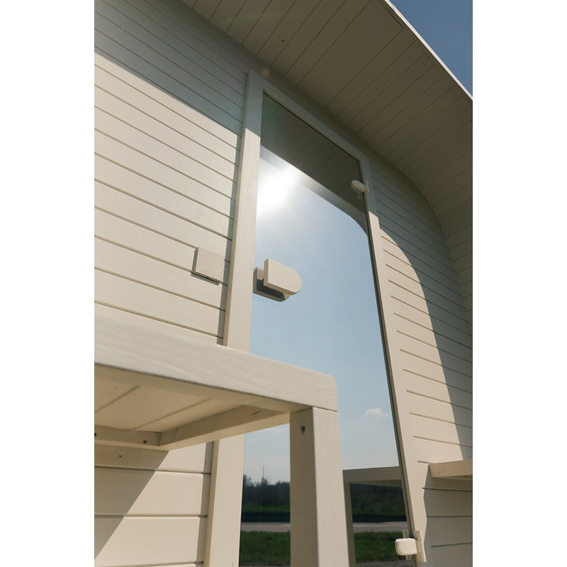 Außenansicht der Ula Large Sauna mit Glastür und heller Holzverkleidung im Sonnenlicht