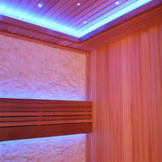 Modernes Saunakabineninterior mit roten Zedernholzwänden, breiter Liege mit Rückenlehne, strukturierter Rückwand und LED-Deckenbeleuchtung in Blau- und Orangetönen