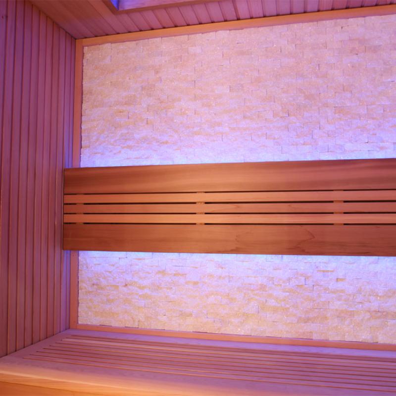 Infrarotkabine mit roten Zedernholzbänken, rosa beleuchtete Rückwand und seitlichen Wandpaneelen, modernes Design mit horizontaler Holzstruktur