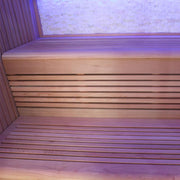 Innenansicht einer modernen Infrarotkabine mit Holzbänken aus roter Zeder und violetter LED-Beleuchtung an Wand und Decke
