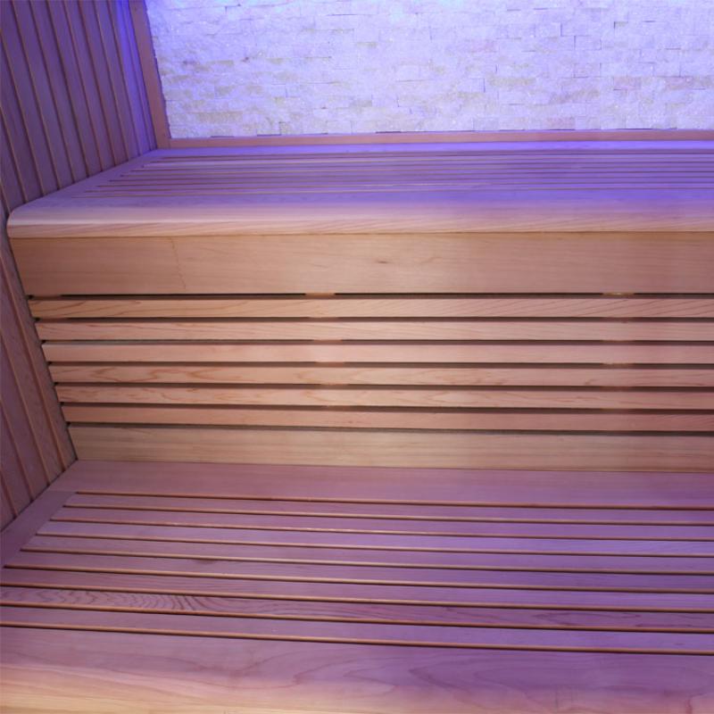 Innenansicht einer modernen Infrarotkabine mit Holzbänken aus roter Zeder und violetter LED-Beleuchtung an Wand und Decke