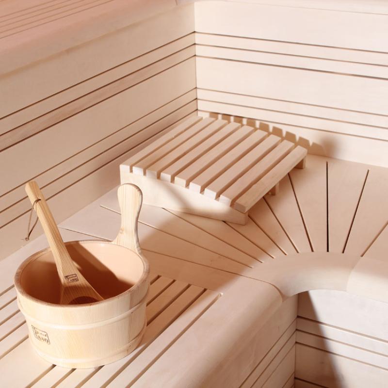 Saunaraum mit heller Zedernholzverkleidung, zwei Holzbänke, Holzaufgusseimer mit Kelle und Kopfstütze aus Holz
