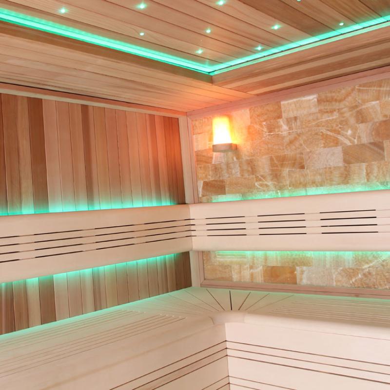 Moderne Sauna aus roter Zeder mit grüner LED-Beleuchtung an Decke und Wand, Salzstein-Panel und hölzernen Sitzbänken im Inneren