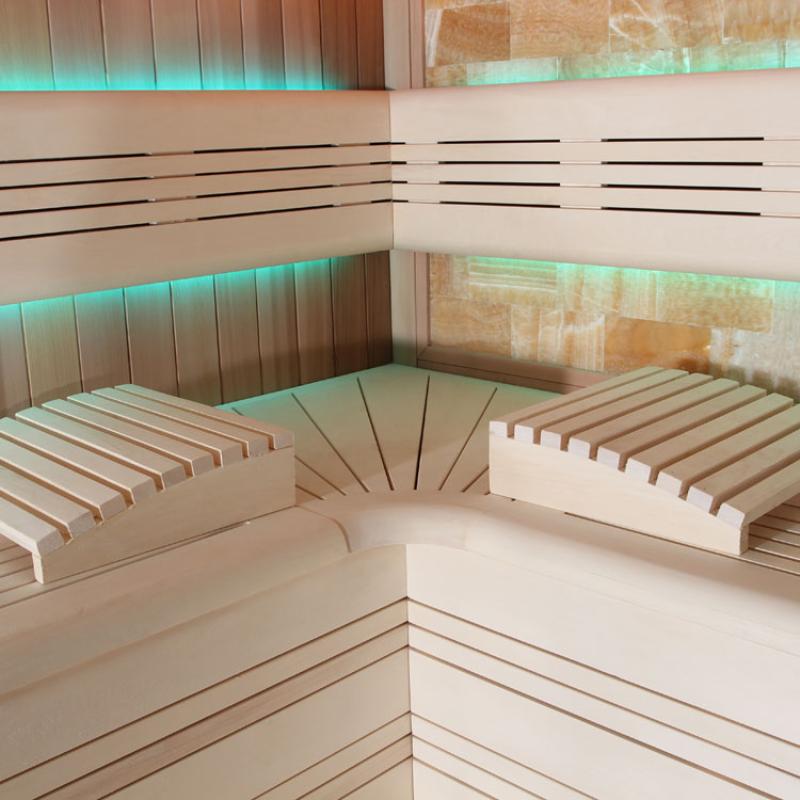 Innenansicht einer modernen Sauna mit Holzbänken aus roter Zeder, türkisem LED-Licht und ergonomischem Design für mehrere Personen.