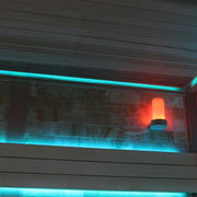 Moderne Sauna-Innenraum mit türkiser LED-Beleuchtung an Wand und Decke sowie roter Leuchte des Saunaofens in der Ecke