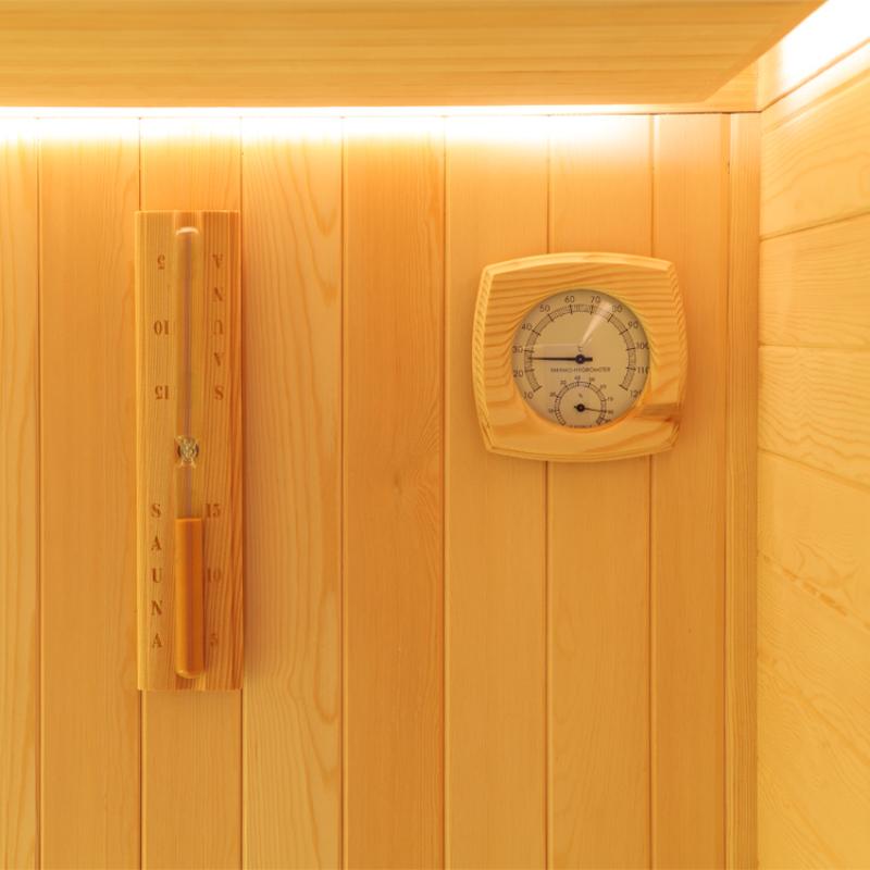 Holzverkleidete Saunakabine mit analógem Thermometer-Hygrometer und vertikalem Saunaofen an der Wand