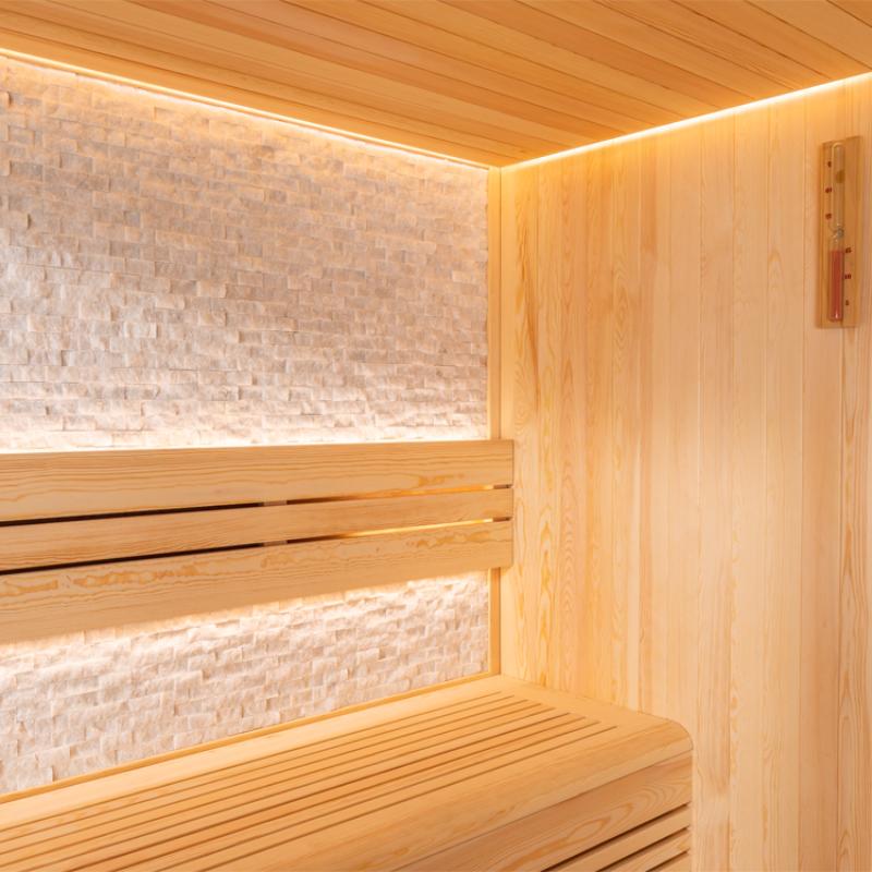 Moderner Saunaraum mit Pinienholzverkleidung, Liege und Rückenlehne, Kristallsteinen an der Wand und indirekter LED-Beleuchtung