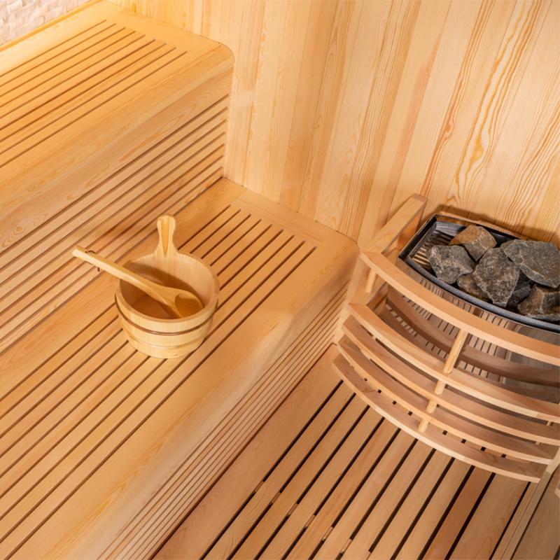 Innenansicht der EAGO AWT E1811B Sauna aus Pinienholz mit Saunabänken, Holzkelle und Saunasteine in der Ecke