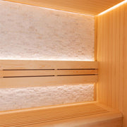Innenraum einer Pinieholz-Sauna mit zwei Liegebänken, Rückenlehne und beleuchteter Kalksteinwand, modernes Design von EAGO