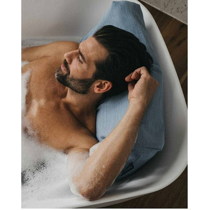 Mann liegt entspannt in der Badewanne mit BADESOFA Rückenkissen in Blau