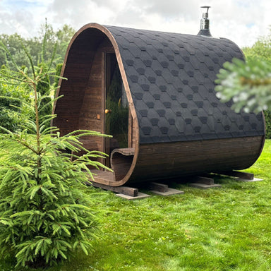  Celsium Herkus Small Gartensauna im Garten bei Sommerwetter, mit elegant geschwungenem Dach und schwarzer Bitumen-Eindeckung.