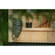 Detailansicht der Celsium Jonas Small Gartensauna – Saunaofen mit Lavasteinen und Saunaeimer auf Lindenholz-Bank, warm beleuchtetes Innenambiente mit natürlichem Holzdesign.