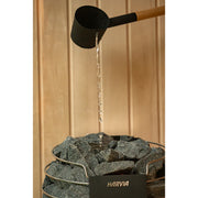 Nahaufnahme Harvia Saunaofen in der Celsium Jonas Small Glassauna – Aufgussmoment mit fließendem Wasser auf heißen Steinen, edle Holzverkleidung im Hintergrund.