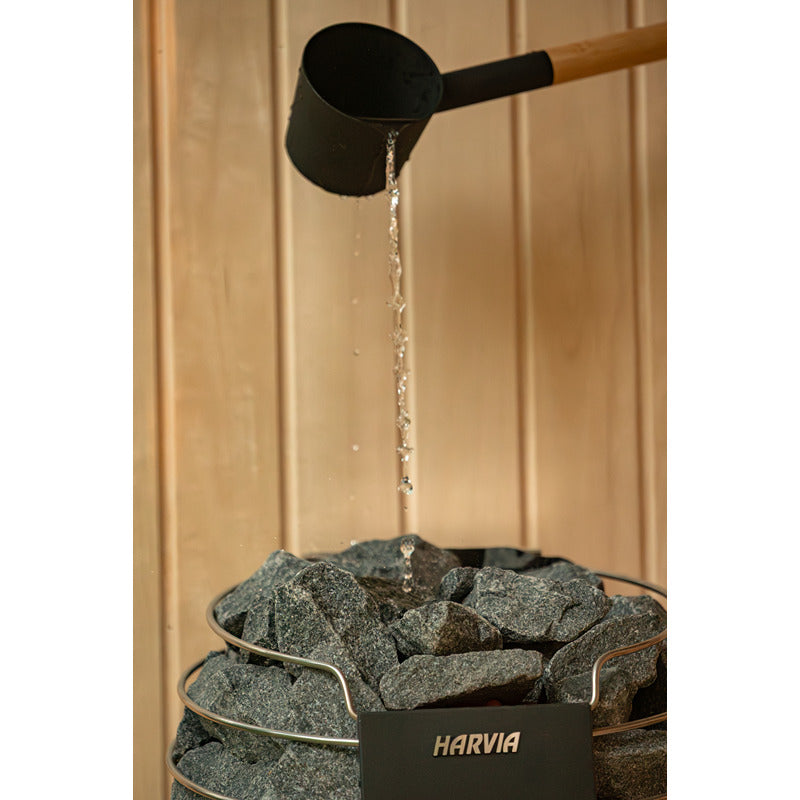 Nahaufnahme Harvia Saunaofen in der Celsium Jonas Small Glassauna – Aufgussmoment mit fließendem Wasser auf heißen Steinen, edle Holzverkleidung im Hintergrund.