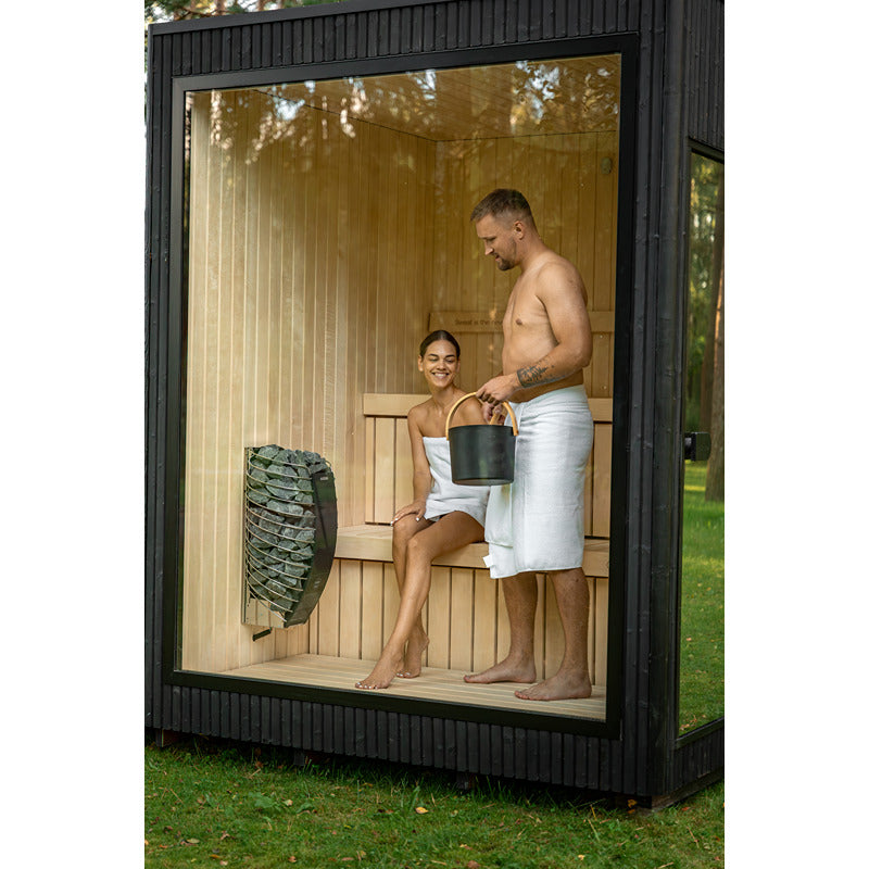 Innenansicht der Celsium Jonas Small Gartensauna – zwei Personen genießen die Wärme auf den Lindenholz-Bänken mit Saunaofen und Glasfront.