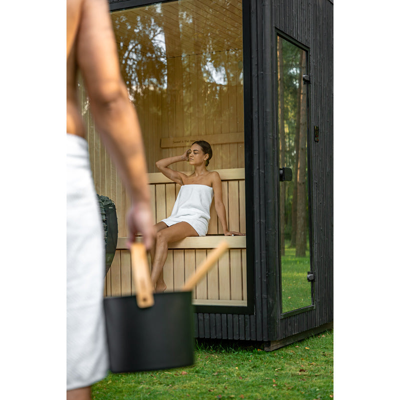 Frau entspannt in der Celsium Jonas Small Glassauna – stilvolle Gartensauna aus Holz mit großem Glasfenster und natürlichem Lichteinfall.
