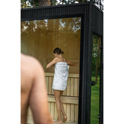 Einstieg in die Celsium Jonas Small Gartensauna – Frau betritt die moderne Glassauna mit hellen Holzflächen und klarer Linienführung.