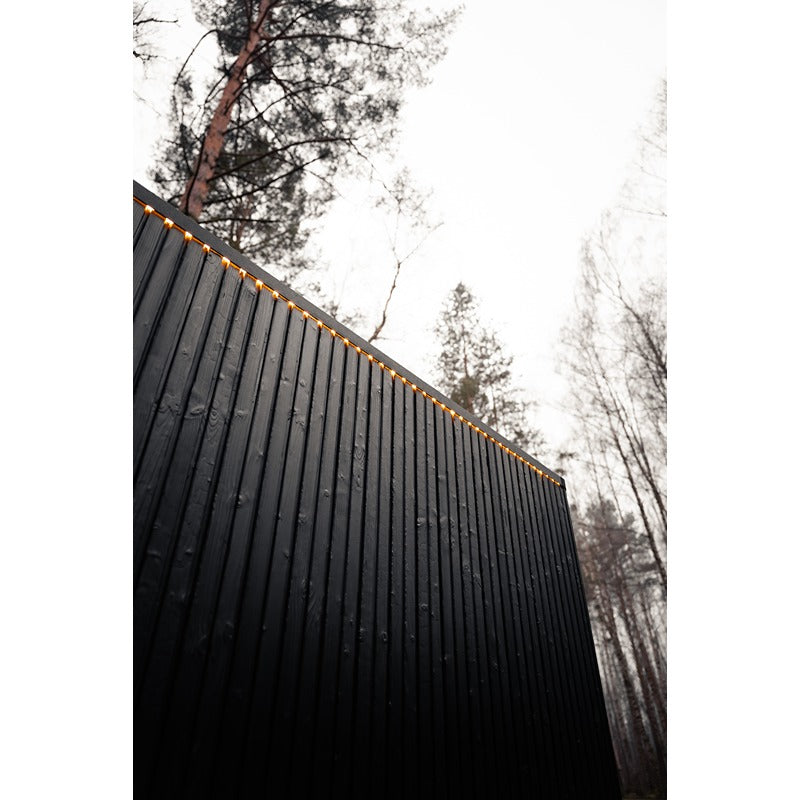 Schwarze Holzfassade der Celsium Jonas Grand Gartensauna mit umlaufender LED-Lichtlinie.
