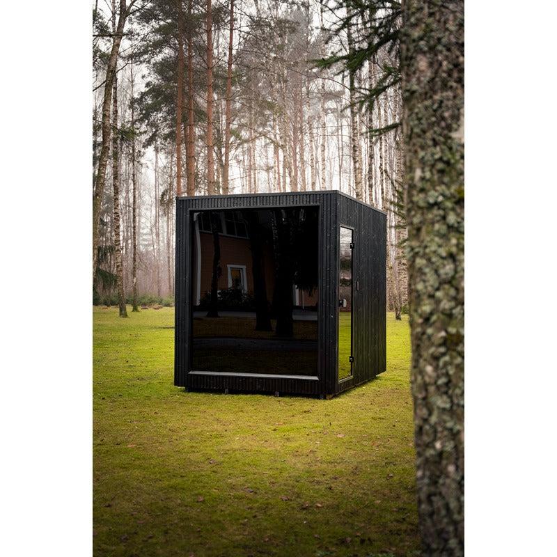Außenansicht der Celsium Jonas Grand Gartensauna mit Glasfront zwischen Bäumen.

