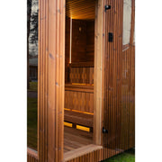 Outdoor-Sauna mit geöffneter Glastür und warm beleuchtetem Holzinterieur.

