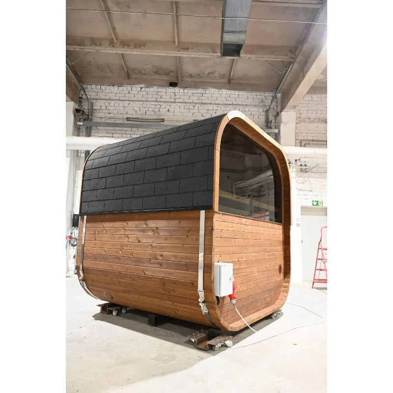 Hekla Cube Sauna mit Holzverkleidung und schwarzen Dachschindeln in Werkstatt, moderne zylindrische Form mit großem Fenster