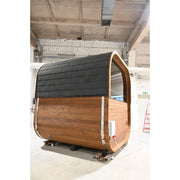 Hekla Cube Fasssauna aus Naturholz mit schwarzem Dach in Werkstatt, moderne zylindrische Saunakapsel mit Holzverkleidung und gerundeter Einstiegsöffnung.