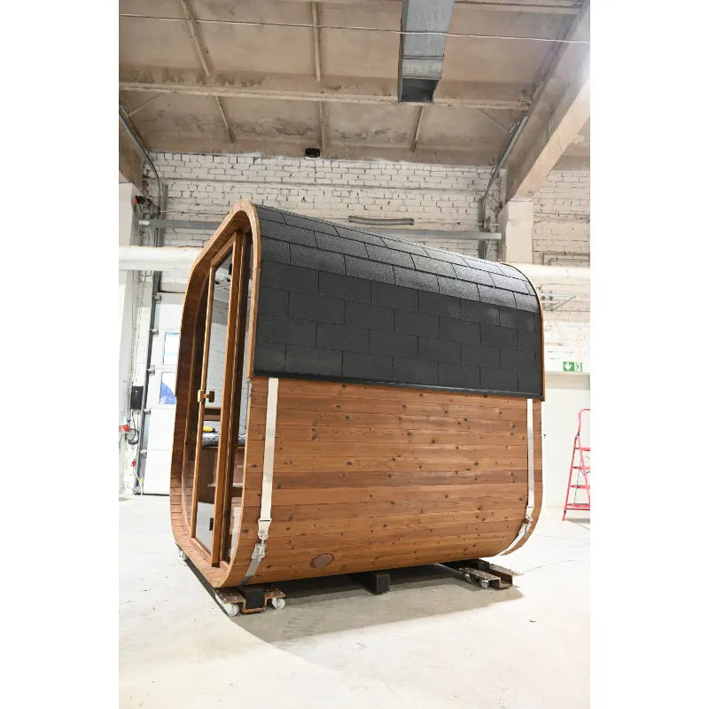 Hekla Cube Fasssauna aus Holz mit schwarzem Dach und geöffneter Tür in einer Werkstatt
