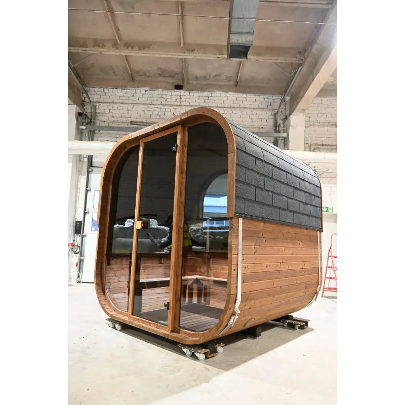 Moderne Fasssauna aus Holz mit großem Glasfenster und abgerundetem Design, auf Rollen in einer Lagerhalle, Innenausstattung sichtbar