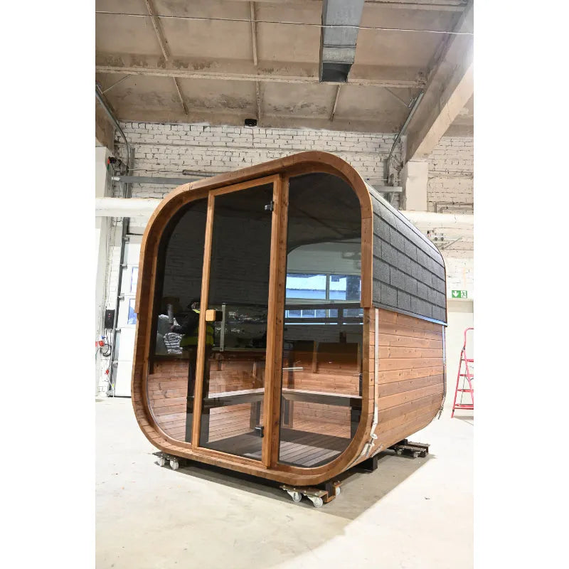 Moderne Hekla Cube Sauna aus Holz mit Glastüren und abgerundeten Ecken in Werkshalle, auf Rollen montiert