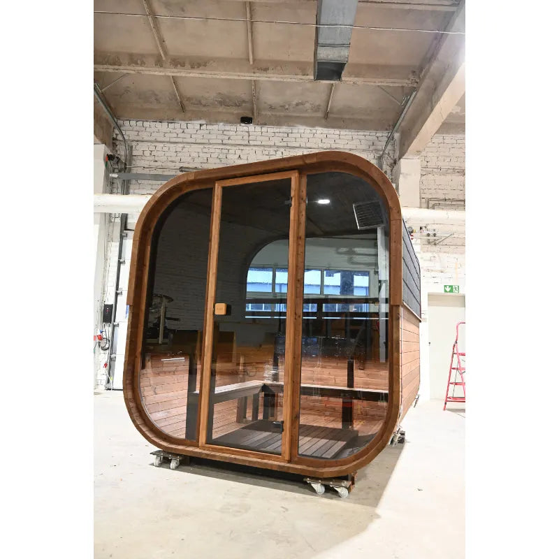 Hekla Cube Sauna aus dunklem Holz mit großen Glastüren und Holzbank in einer Produktionshalle