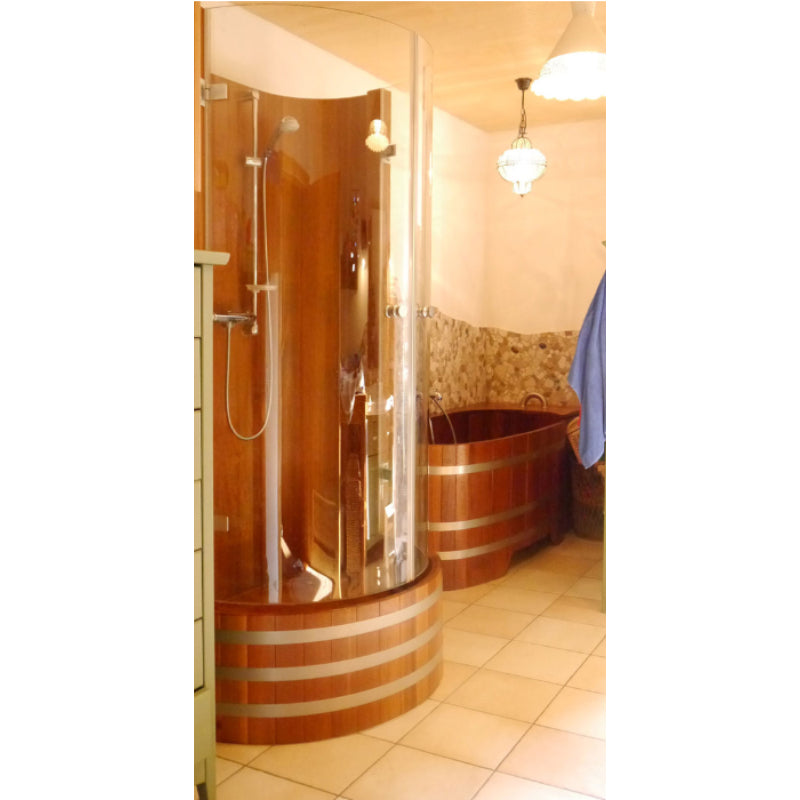 Blumenberg Holz-Duschkabine aus Western Red Cedar mit geschwungener Glasfront und Metallbändern, daneben ein Holz-Badebottich in eleganter Wellness-Umgebung