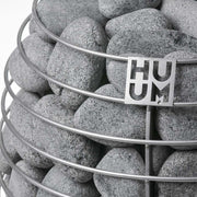  HUUM Saunaofen mit gefülltem Steinkorb aus Olivin-Diabas – runde Saunasteine und Edelstahl-Logo in Nahaufnahme