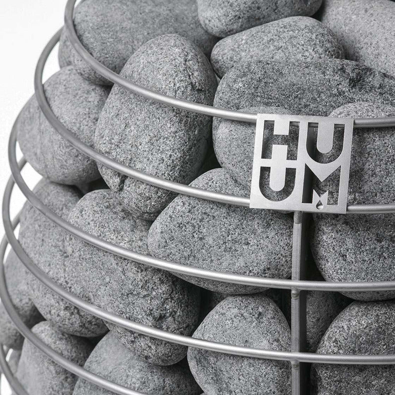  HUUM Saunaofen mit gefülltem Steinkorb aus Olivin-Diabas – runde Saunasteine und Edelstahl-Logo in Nahaufnahme