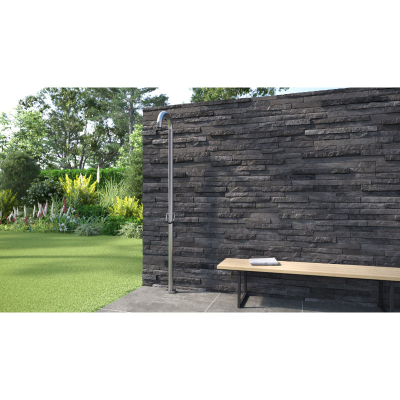 Outdoor-Dusche JEE-O Original 01 mit Edelstahl-Duschkopf an schwarzer Natursteinmauer, Holzbank und grüner Gartenlandschaft.