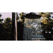 Outdoor-Dusche JEE-O Original mit großem Regenduschenkopf in schwarzem Design, Wasserstrom vor natürlichem Grün und Baumfolie.