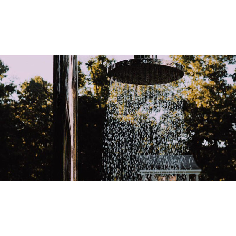 Outdoor-Dusche JEE-O Original mit großem Regenduschenkopf in schwarzem Design, Wasserstrom vor natürlichem Grün und Baumfolie.