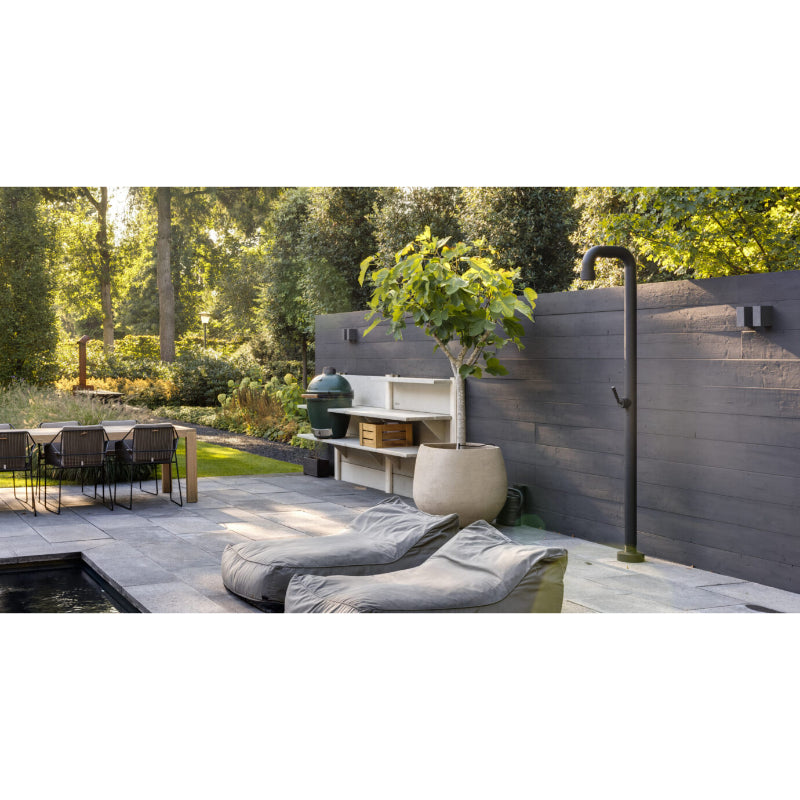 Moderne Gartendusche JEE-O Soho 01 mit schwarzem Rahmen auf eleganter Terrasse, umgeben von Liegestühlen und Designmöbeln in natürlicher Waldumgebung.