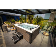 Platinum Spas Topaz Outdoor Whirlpool mit sprudelndem Wasser auf überdachter Terrasse, umgeben von Pflanzen und Loungebereichen mit Meerblick