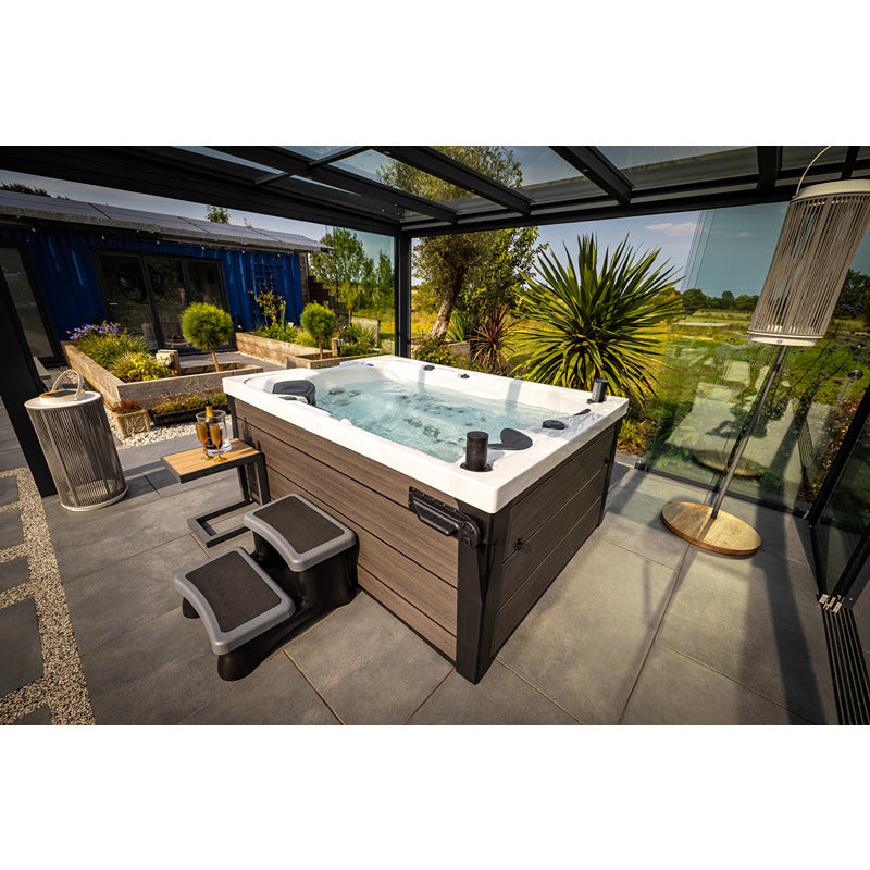 Platinum Spas Topaz Outdoor Whirlpool mit sprudelndem Wasser auf überdachter Terrasse, umgeben von Pflanzen und Loungebereichen mit Meerblick