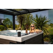 Frau entspannt in modernem Platinum Spas Topaz Outdoor-Whirlpool unter Glasdach mit Blick auf grüne Gartenlandschaft und Palme.
