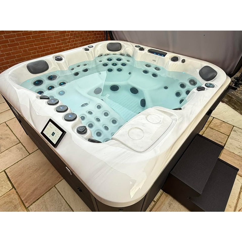 Platinum Spas Florence Outdoor Whirlpool mit weißem Kunststoffgehäuse, türkisblauem Wasser, zahlreichen Massagedüsen und komfortablen Rückenlehnen an Ziegelsteinmauer.