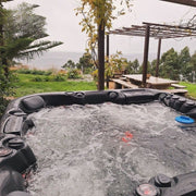 Platinum Spas Florence Outdoor Whirlpool mit schwarzem Rand in Gartenlandschaft mit Meerblick, umgeben von Pflanzen und Holzpergola