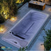 Eingelassener Mini Pool Hades Pro von Platinum Spas in Sterling Silver bei stimmungsvoller Gartenbeleuchtung auf moderner Terrasse mit Esstisch aus Holz.