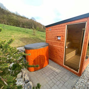 Polar Spa Standard Eisbad aus orangem Thermoholz neben rotem Saunahaus in parkähnlicher Gartenlandschaft