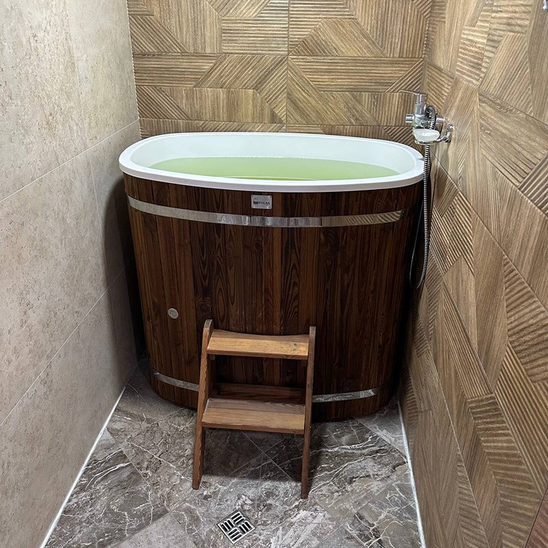 Eisbad aus dunklem Thermoholz mit weißem Innenrand, gefüllt mit grünem Wasser, in moderner Badezimmerecke mit geometrischen Holzfliesen und Holztreppe